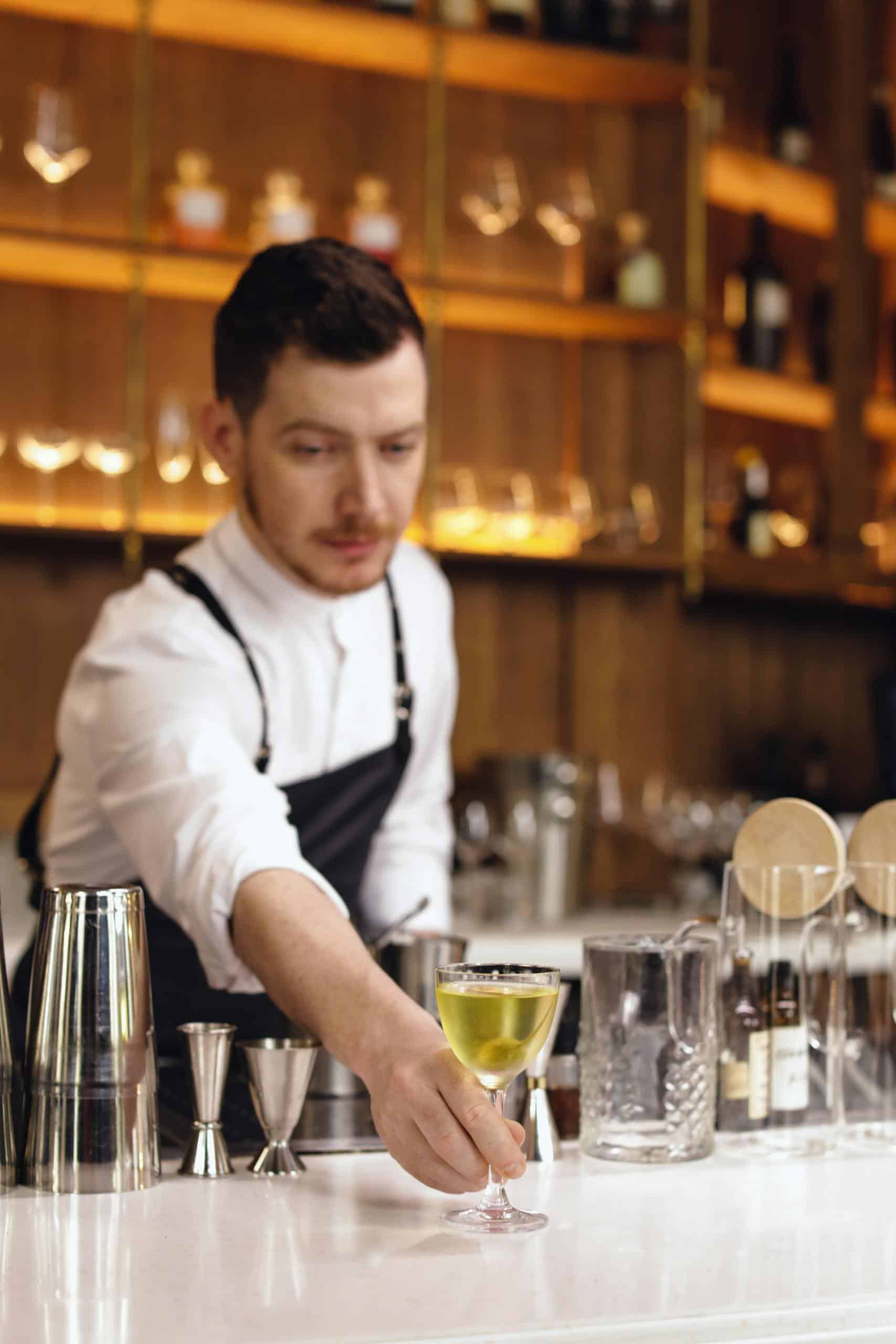 Bartender presenting a cocktail in a modern and elegant bar setting.