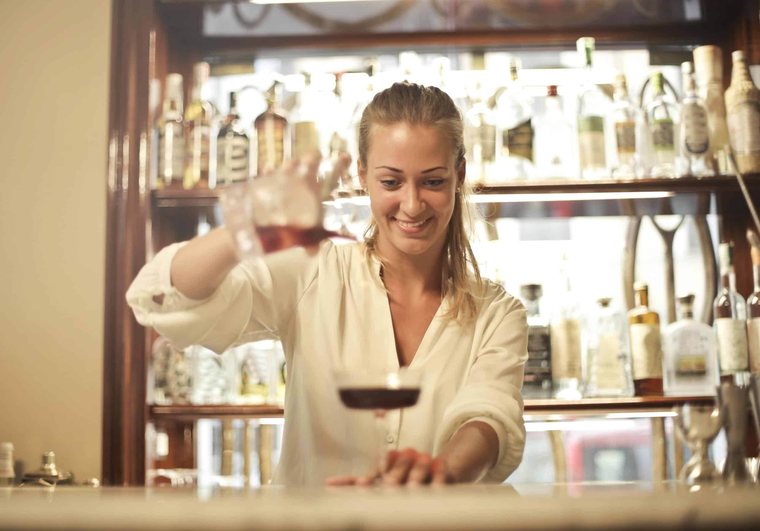 Cheerful bartender pouring a cocktail with a smile at a lively bar.