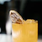 Close-up of a refreshing citrus cocktail garnished with a dried orange slice, served in a clear glass.