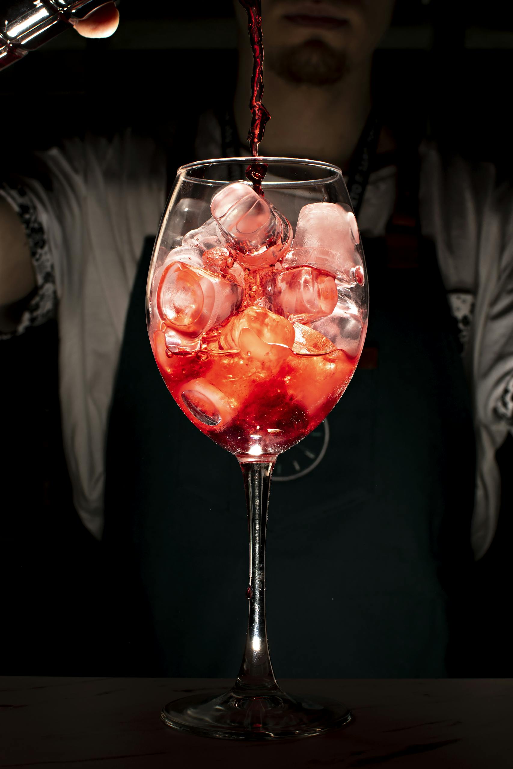 Vibrant cocktail pour into an ice-filled wine glass by a bartender, highlighting the drink's color and texture.